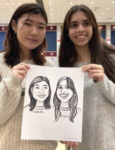 Two women holding caricature drawings of themselves.