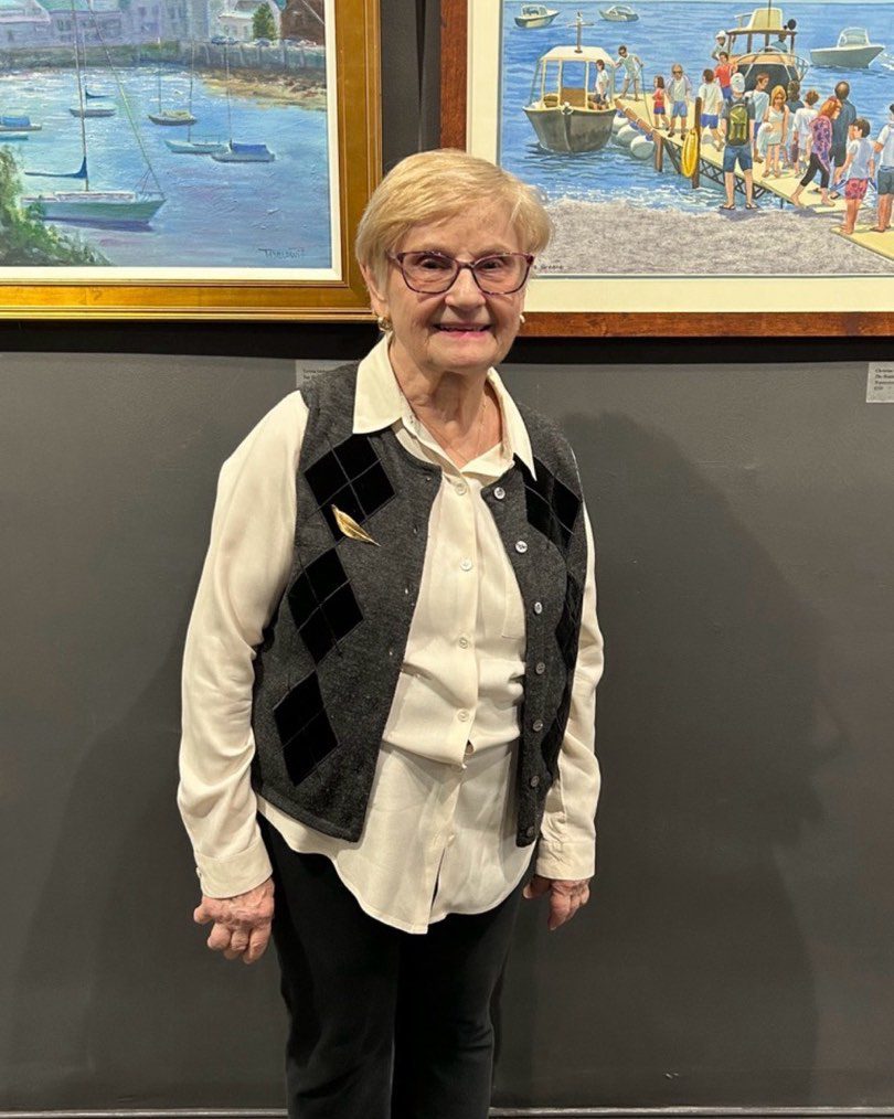 Woman in a vest standing in front of paintings.